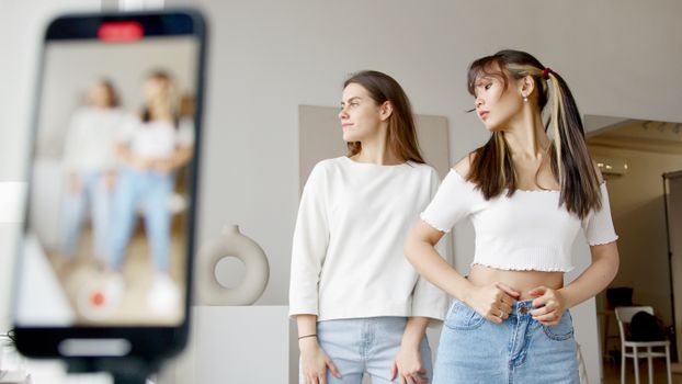Two women recording dance moves on a smartphone indoors, showcasing lifestyle creativity.