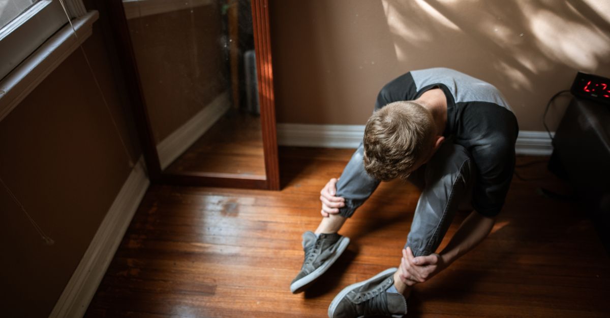 A person kneeling on a rough wooden floor, head down, with soft light coming through a window
