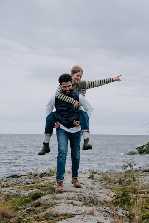 Man Carrying a Woman on His Back on the Seashore and Smiling 