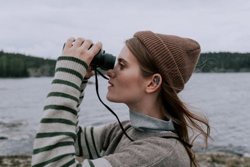 Woman in Knitted Cap and Sweater Using a Black Binoculars