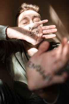 A young man covering his face with hands, displaying messages of distress and a plea to stop.