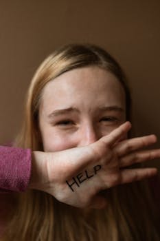 A distressed teenager covering face with 'HELP' written on hand, signifying need for support.