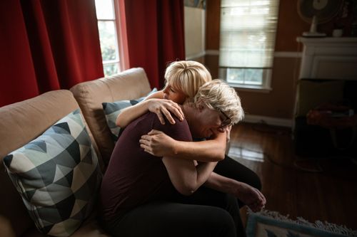 Free An emotional and supportive embrace between a couple on a sofa, showcasing affection and togetherness in a cozy home setting. Stock Photo