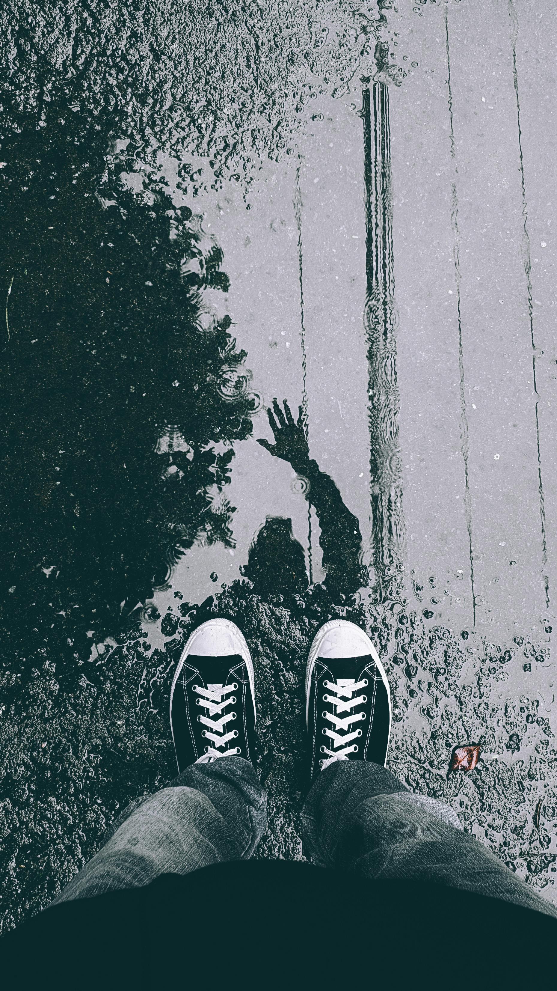 person in black sneakers standing on puddle and waving in reflection