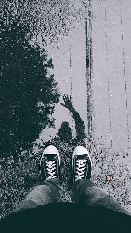 Person in Black Sneakers Standing on Puddle and Waving in Reflection