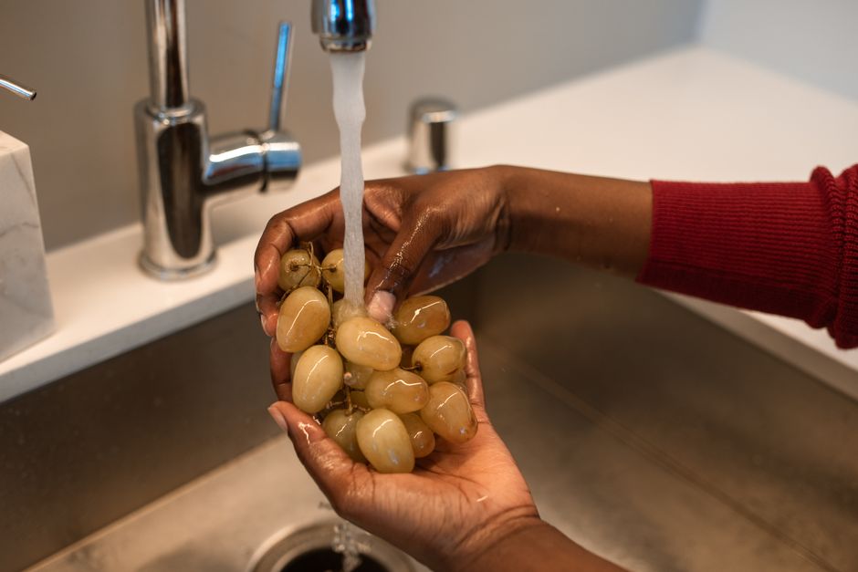 Close-up of hands washing grapes under a kitchen faucet, emphasizing cleanliness.