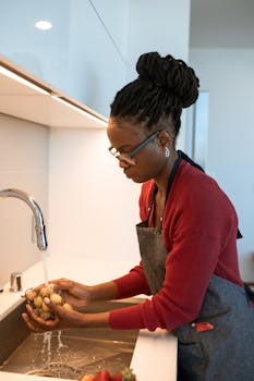 African American woman washing grapes in a modern kitchen with apron and eyeglasses.