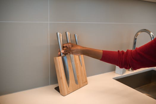 A person retrieving a knife from a wooden kitchen block on a countertop.