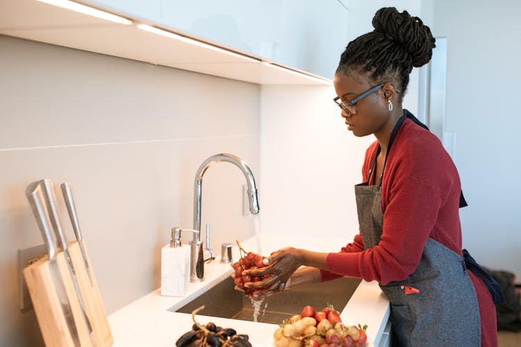 A Woman In Red Long Sleeves Washing Fruits