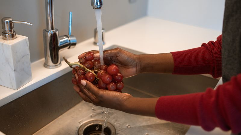 Homeowner rinsing a small mesh heat pump water heater air filter under a kitchen faucet