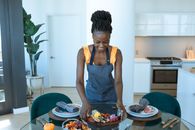 Adult woman arranging a charcuterie board on a dining table in a stylish kitchen setting.