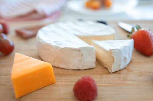Free A wooden board featuring brie, cheddar cheese, and fresh fruits for tasting. Stock Photo