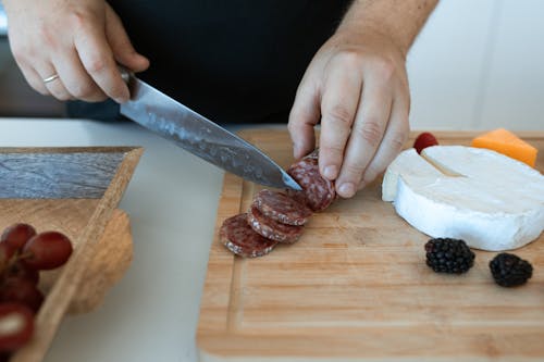 A Person Slicing Salami on a Wooden Chopping Board