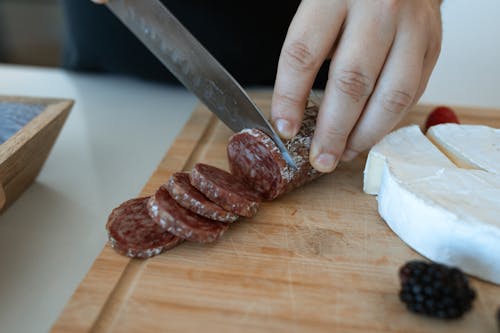 Free Close-Up Shot of a Person Slicing Salami on Wooden Chopping Board Stock Photo