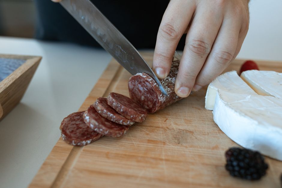 A log of summer sausage sliced into rounds and fanned out on a wooden board next to cubed cheddar and crackers