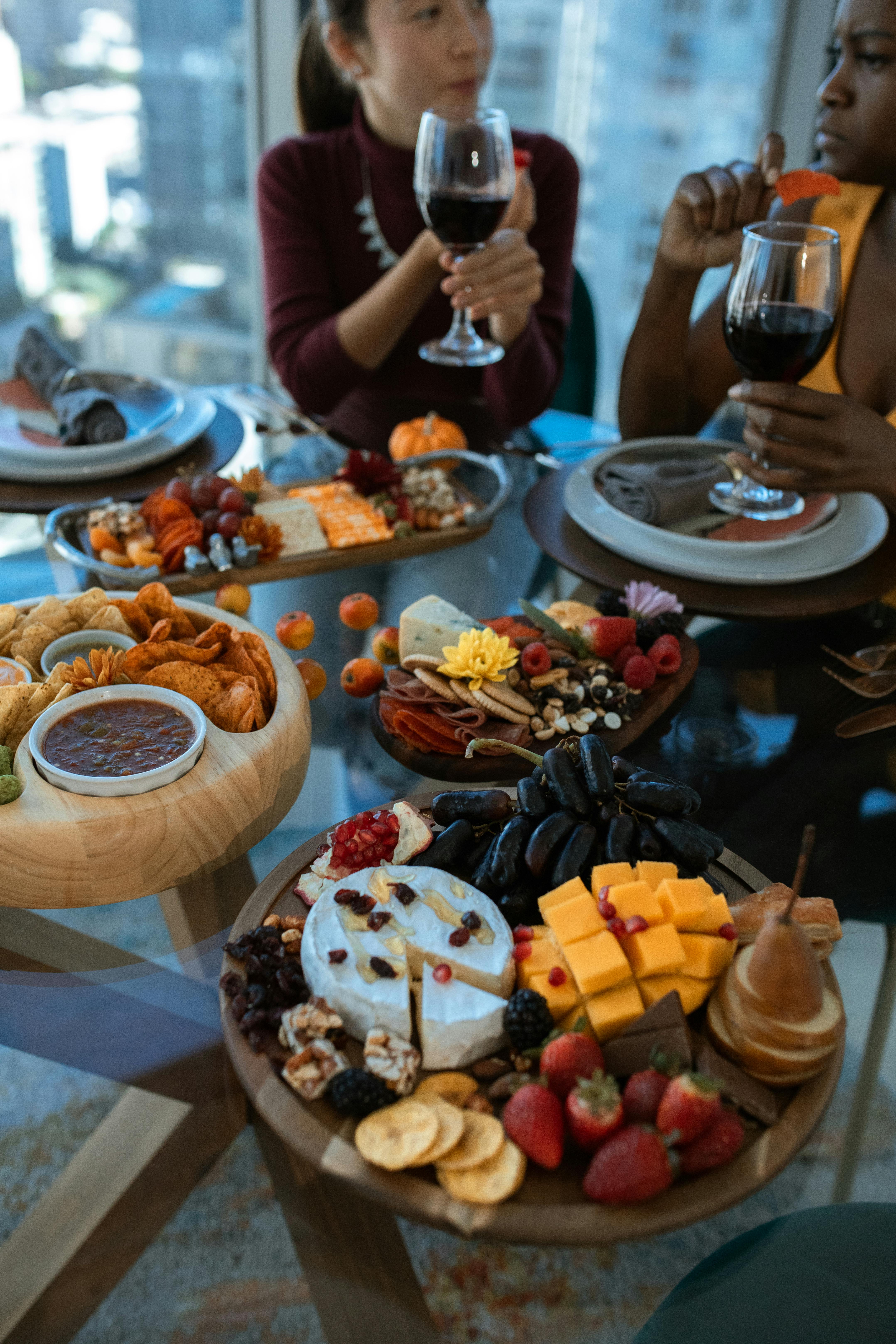 Two women enjoying a sophisticated charcuterie board with wine in a modern indoor setting.