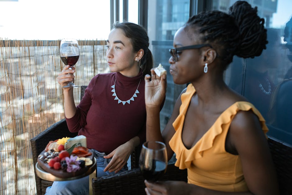 Two women savoring cheese and wine on a balcony, capturing a moment of leisure and friendship.