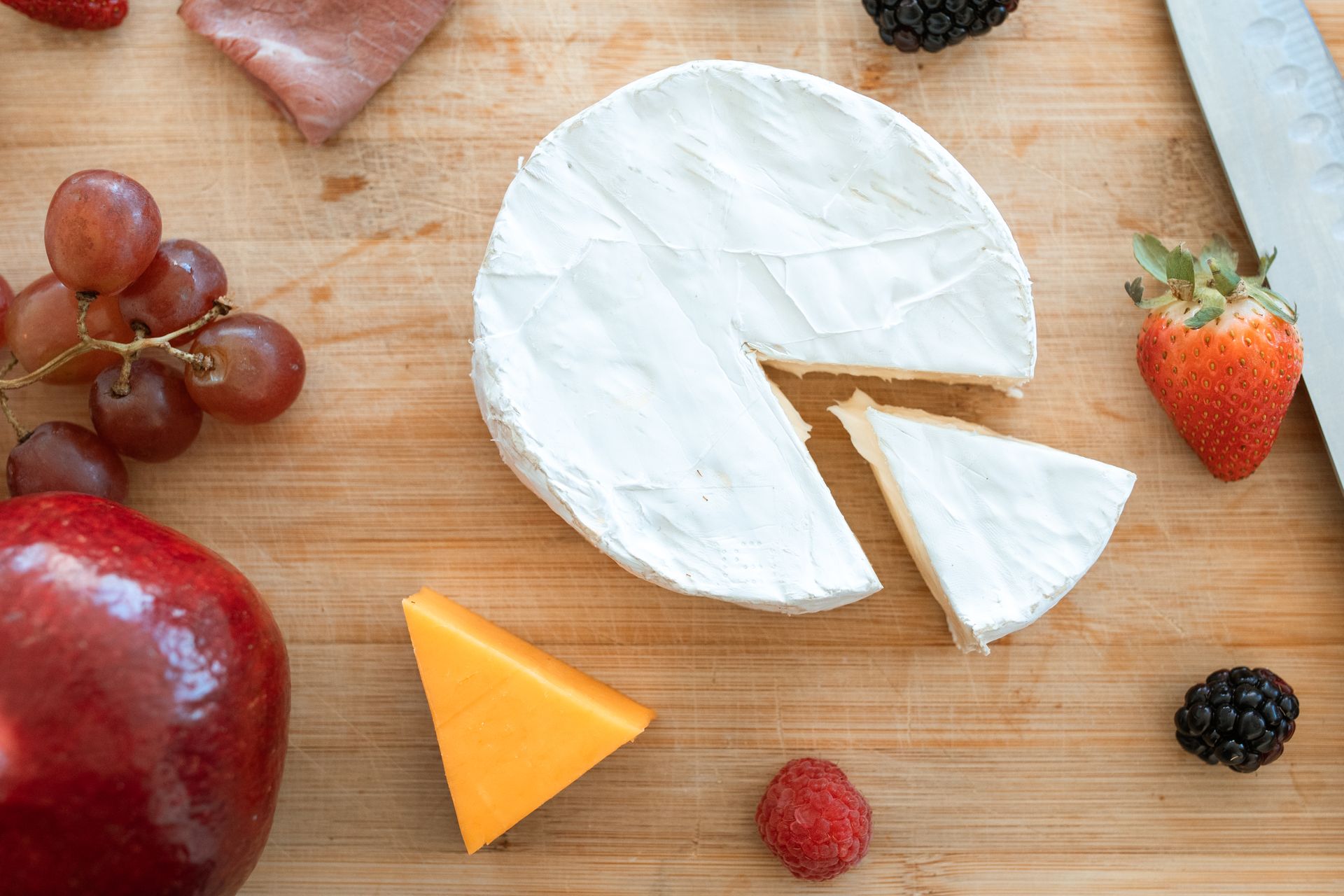 Delicious assortment of brie cheese with fresh fruits on a wooden surface, perfect for gourmet presentations.