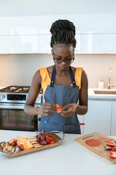 African American woman in kitchen preparing a charcuterie board with fruits and cheese.
