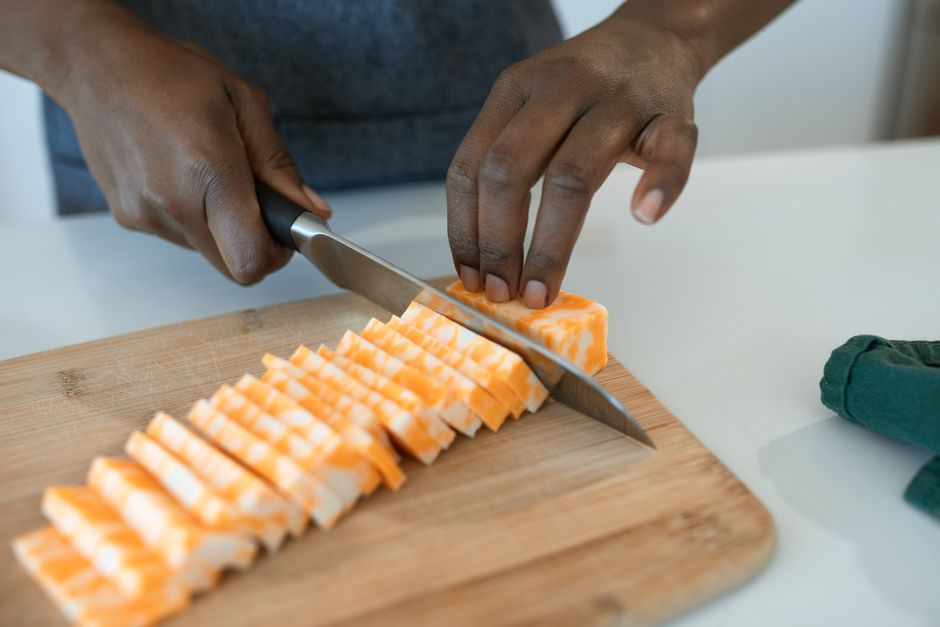 Close-up of hands slicing cheese on a wooden board in a modern kitchen setting.