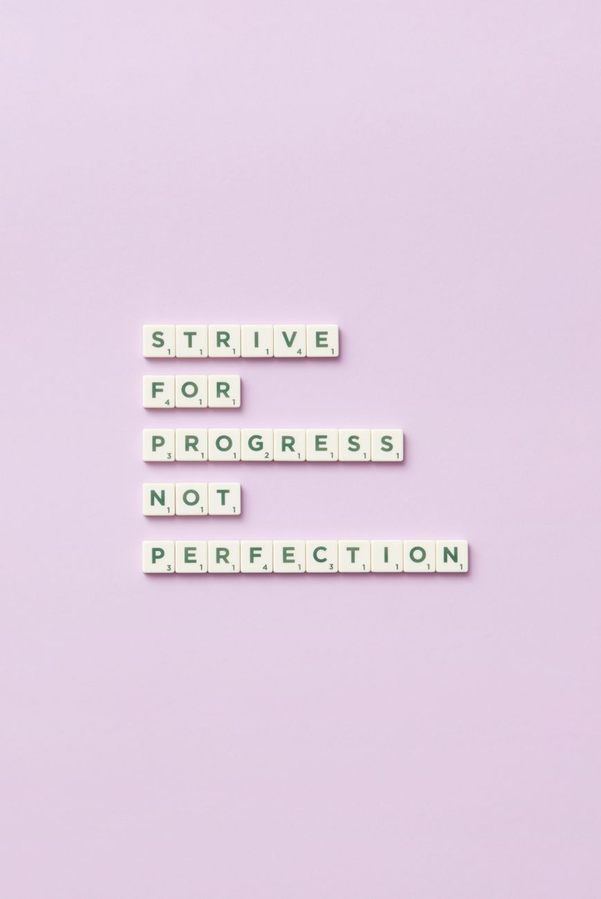 Scrabble tiles spelling 'Strive for progress, not perfection' on a pastel background.