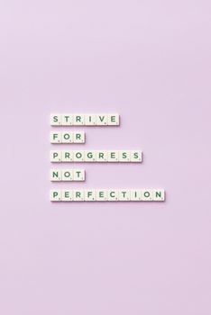 Scrabble tiles spelling 'Strive for progress, not perfection' on a pastel background.