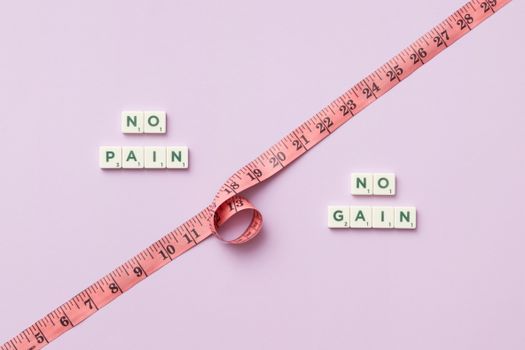 Pink tape measure with 'No Pain No Gain' spelled in Scrabble tiles on pink background.