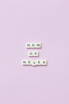 Inspirational message 'Now or Never' using Scrabble tiles on a pastel background.