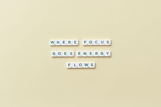 Inspirational quote 'Where Focus Goes Energy Flows' spelled with Scrabble tiles on a minimalist background.