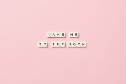 Scrabble letters arranged to say 'Take Me to the Moon' on a pink background.
