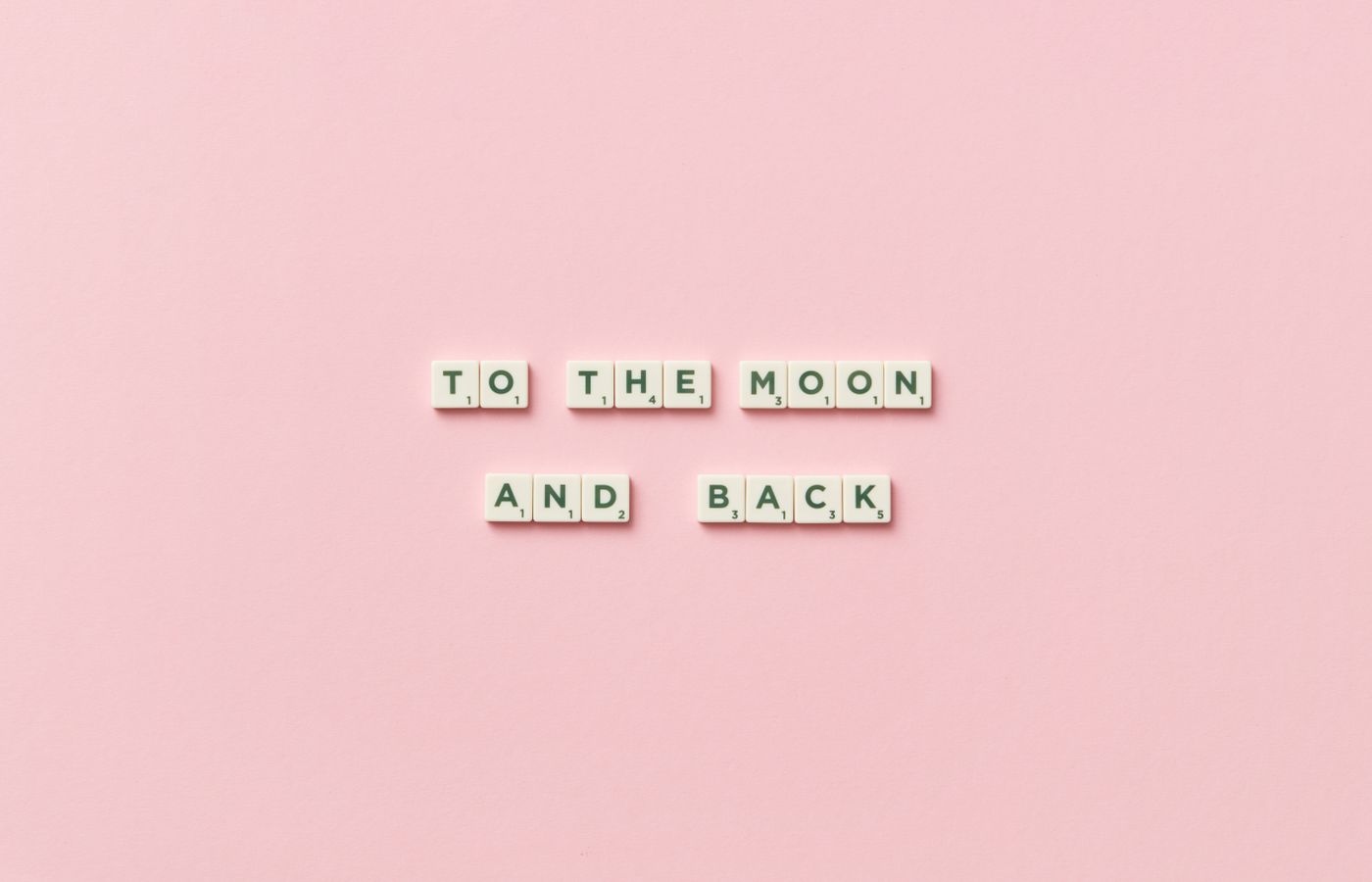 Scrabble tiles spelling 'To the Moon and Back' on a pastel pink background.