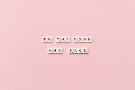 Scrabble tiles spelling 'To the Moon and Back' on a pastel pink background.
