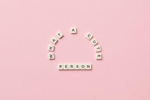 Free Flatlay of Scrabble tiles spelling 'What a cute person' on a pastel pink background. Stock Photo