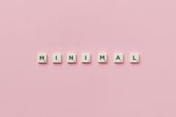 Scrabble tiles spelling 'minimal' on a pink background, showcasing minimalist design.