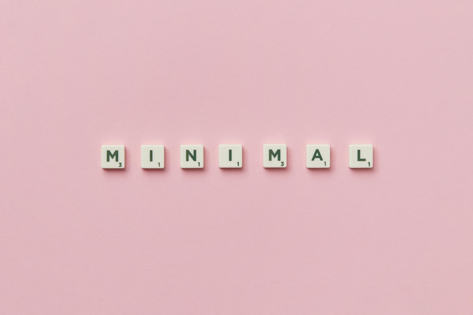 Scrabble tiles spelling 'minimal' on a pink background, showcasing minimalist design.