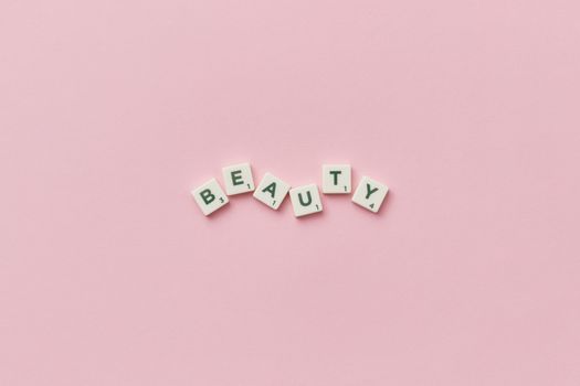 Scrabble tiles forming the word 'Beauty' on a soft pink background, top view, minimalist style.