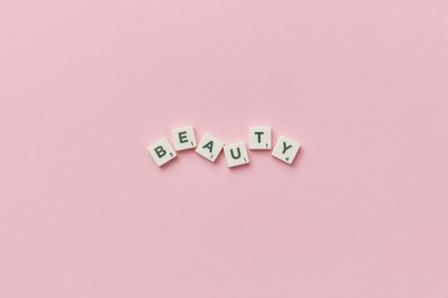 Free Scrabble tiles forming the word 'Beauty' on a soft pink background, top view, minimalist style. Stock Photo