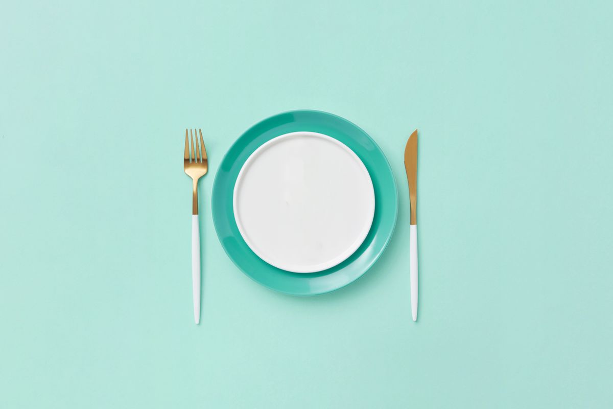 Plato vacío con tenedor y cuchillo sobre fondo turquesa, que evoca las horas de ayuno de una ventana de alimentación