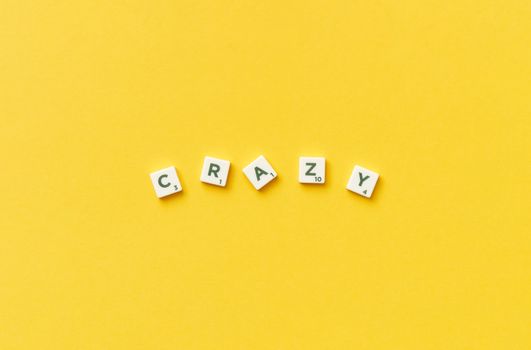 Scrabble tiles spelling 'crazy' on a vibrant yellow background.