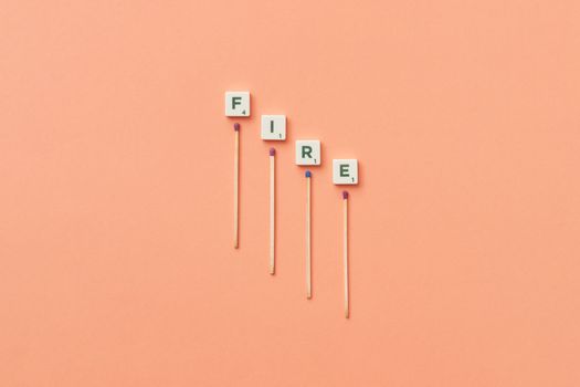 Fire spelled with matches and tiles on an orange background, conceptual image.