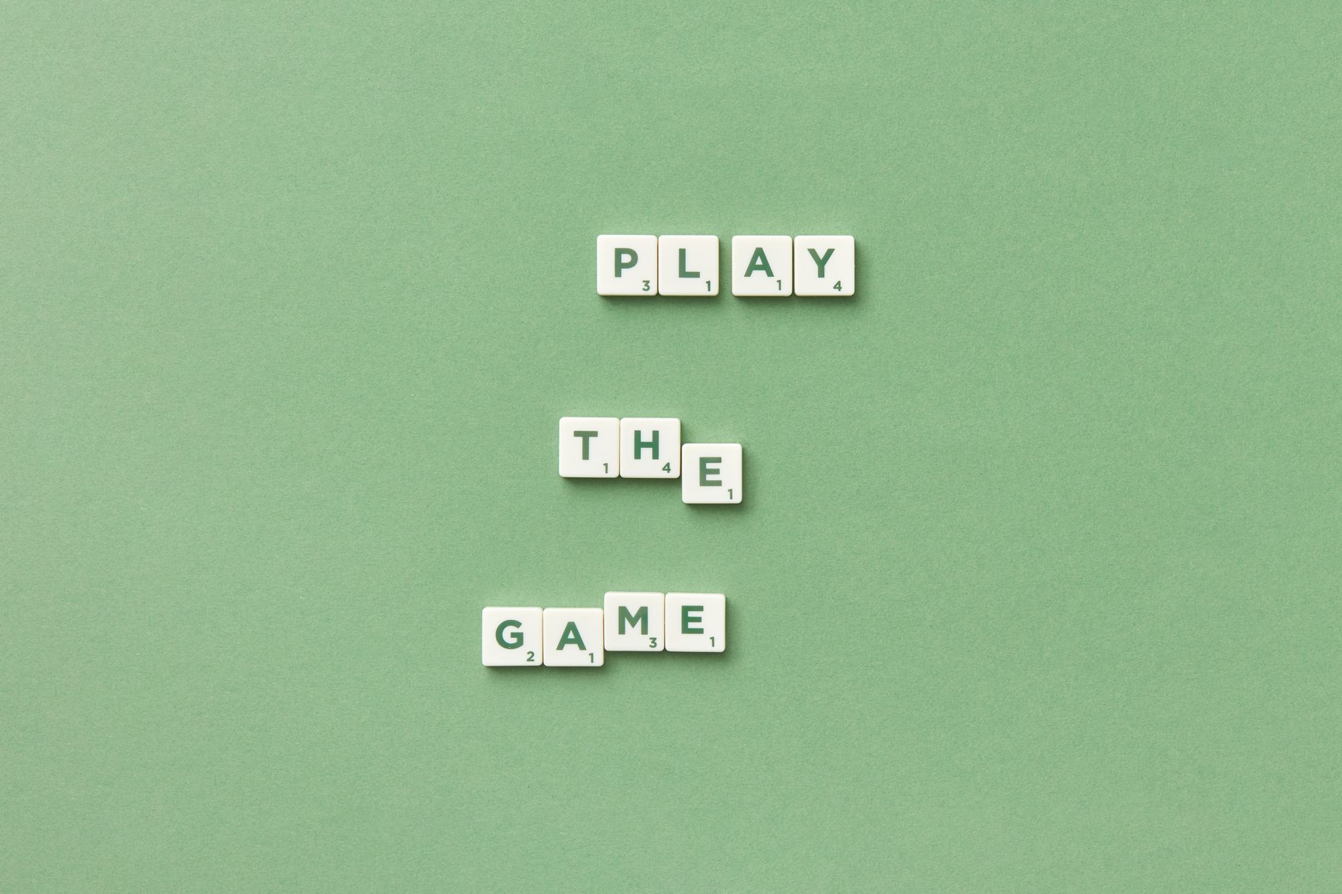 Scrabble letter tiles spelling 'Play the Game' on light green background.