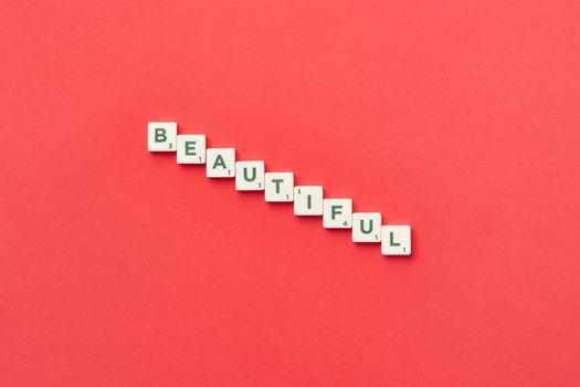 Scrabble tiles arranged to spell 'Beautiful' on a vibrant red background, highlighting letters and creativity.