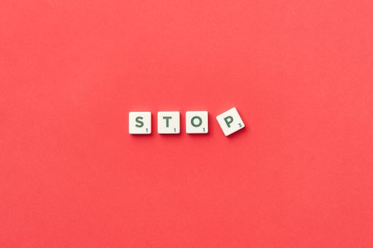 Scrabble tiles spelling 'STOP' on a vivid red background, viewed from above.