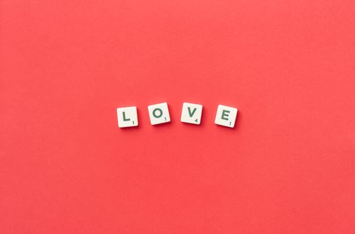 Free Scrabble tiles spelling "LOVE" on a vibrant red background, viewed from above, perfect for romantic themes. Stock Photo