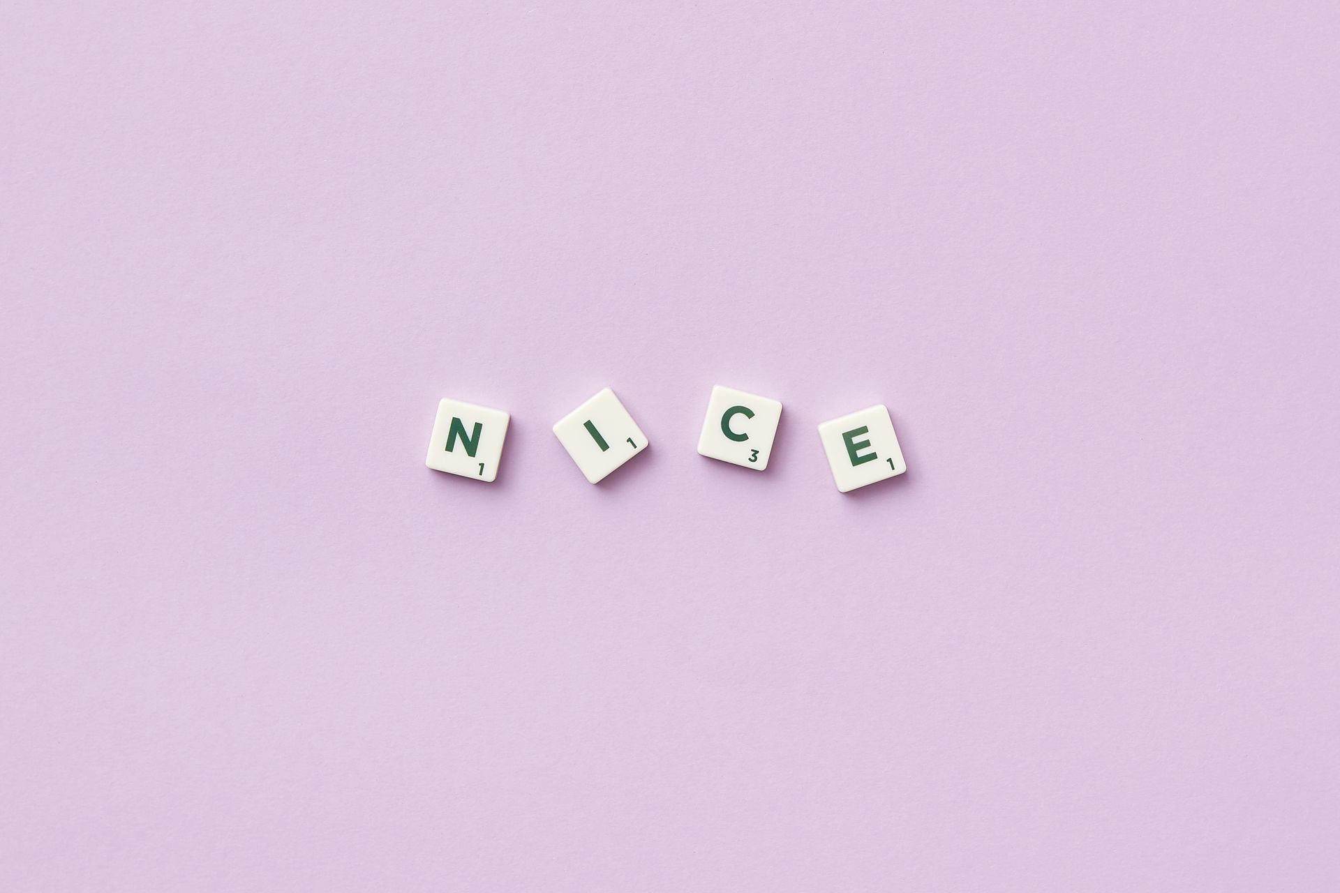 Scrabble tiles spell 'nice' on a minimalist purple surface, playful and simple design.