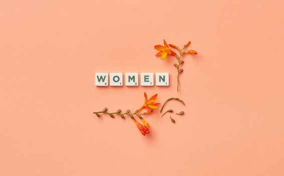 Scrabble tiles spelling 'Women' surrounded by orange flowers on a pink background.