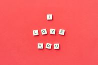 Scrabble tiles arranged to spell 'I Love You' on a vibrant red background, top view.