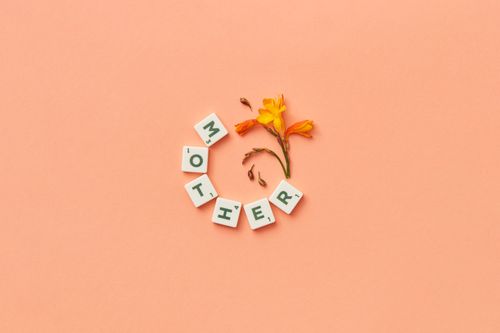 Free Scrabble tiles spelling 'mother' with flowers on peach background, perfect for Mother's Day. Stock Photo