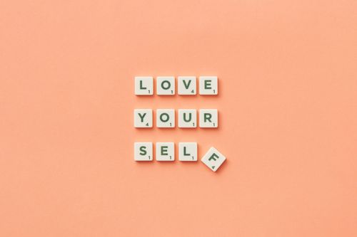 Free Scrabble tiles spelling 'Love Yourself' on a peach background, inspiring self-care. Stock Photo