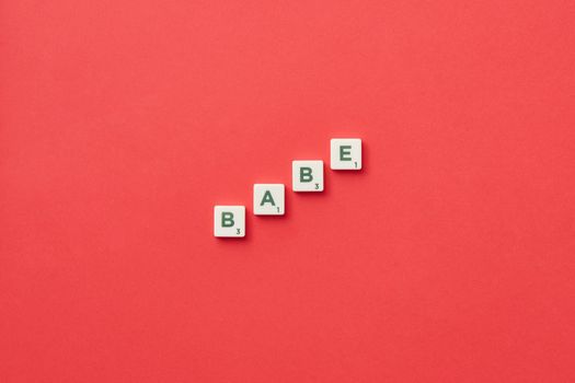 Scrabble letter tiles spell 'babe' on a vibrant red background, viewed from above.